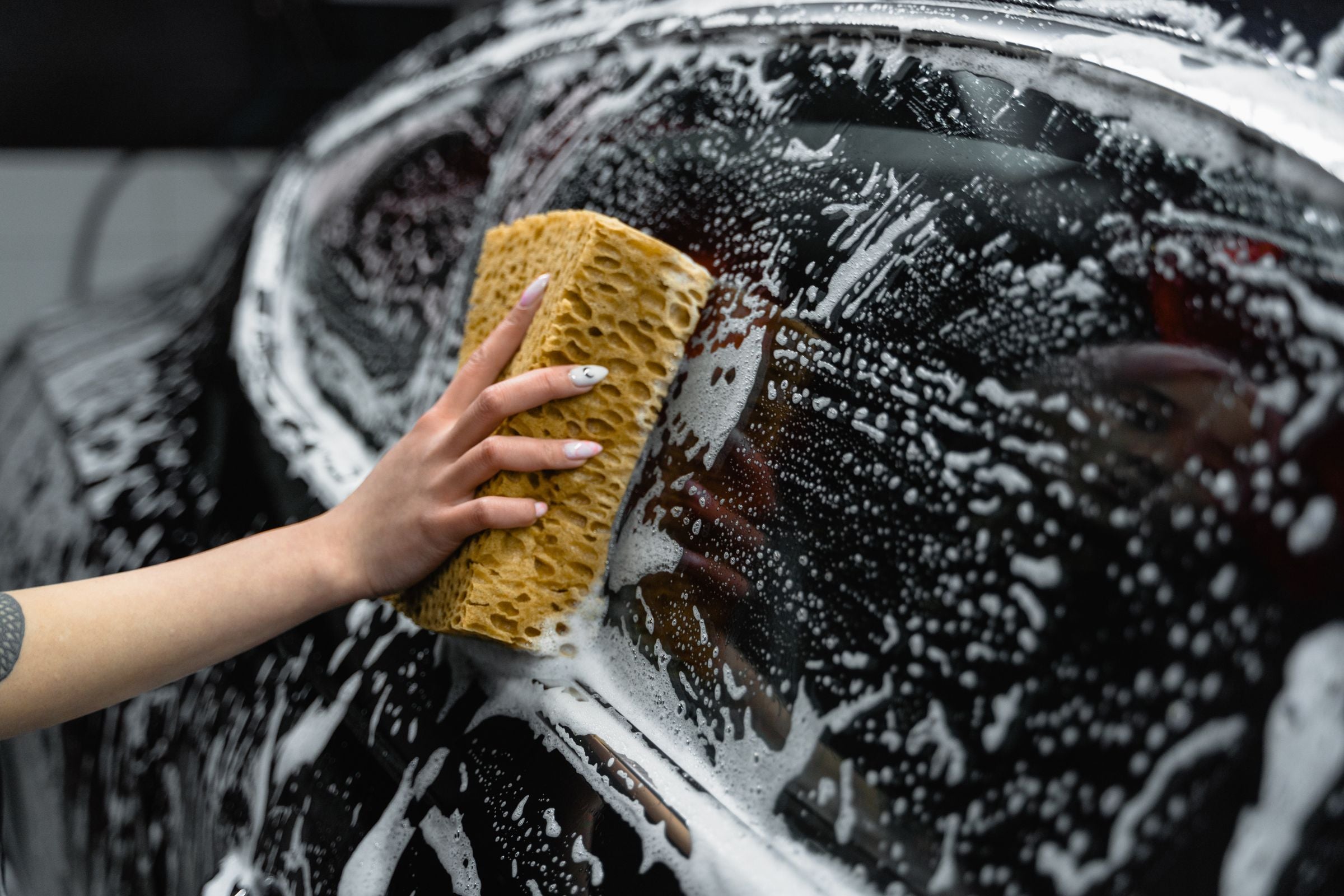 Hand washing a dark car with a sponge and foam